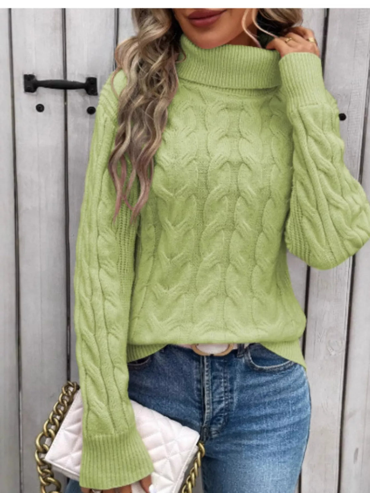 Woman wearing a light green cable knit turtleneck sweater with jeans